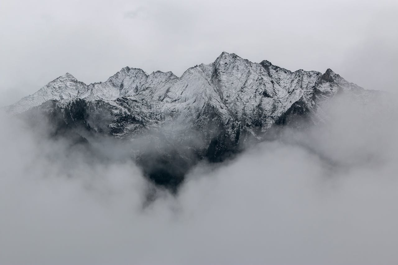A breathtaking view of snow-covered mountain peaks surrounded by dense fog, creating a mystical landscape.